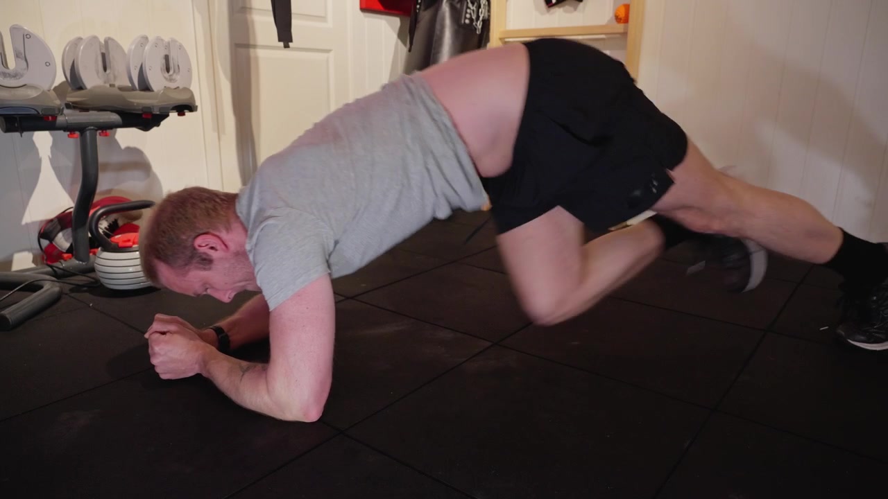Un uomo in posizione plank esegue mountain climbers, spingendosi fino all'esaurimento in una palestra domestica