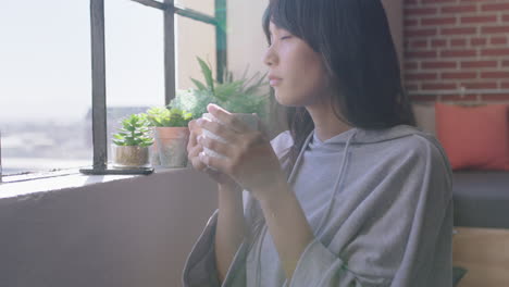 beautiful young asian woman drinking coffee at home enjoying relaxed morning looking out window planning ahead thinking contemplative female in trendy apartment