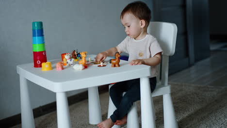 pretty little boy plays with toys sitting at desk. lovely one year old child studying animals.