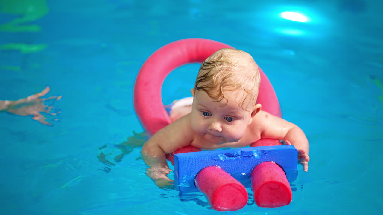 Cute infant baby swimming on the pool foams tick. Close up. Swimming lessons for newborn.