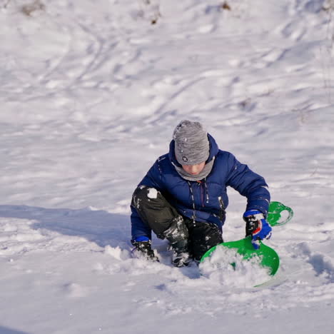 child boy having fun, playing with plastic sledge while having snowy winter walk in nature. frost winter season. cute little boy with spade plays with snow on a winter day. winter games and fun