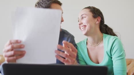 una joven pareja caucásica hablando y pagando sus cuentas usando una computadora portátil