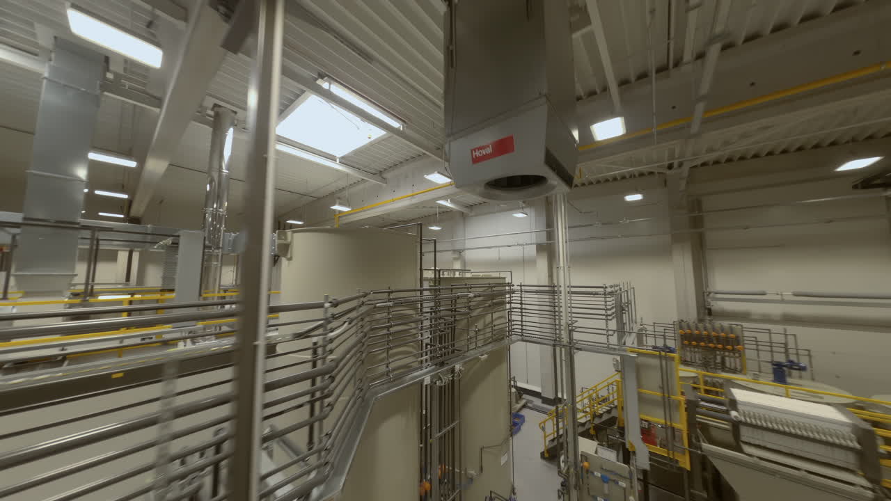 FPV-droneoptagelser, der flyver dynamisk gennem transportsystemerne på en pulverlakeringfabrik. Kameraet snoer sig mellem ophængte metaldele, der bevæger sig langs produktionslinjer, og fanger den industrielle stemning
