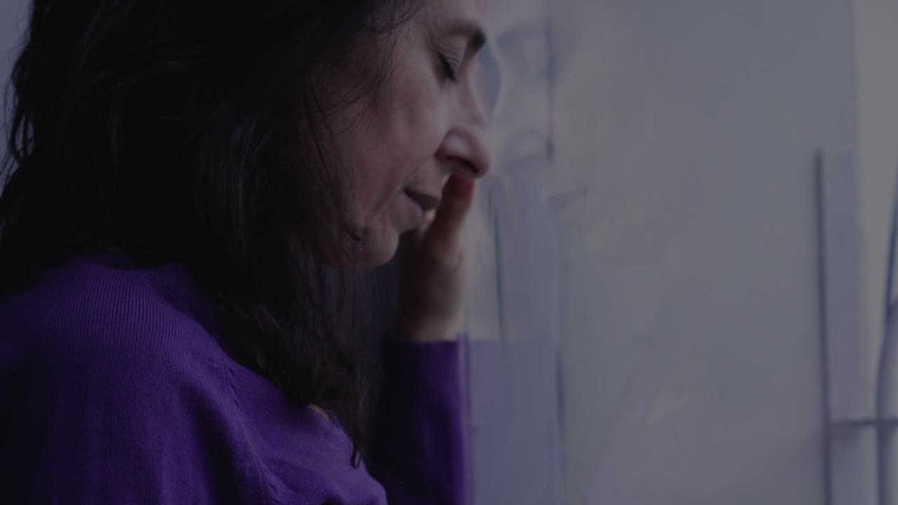 Sola nelle avversità: Donna stressata riflessa su una finestra mentre affronta delle sfide.