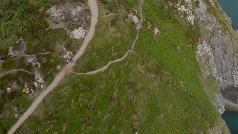 imagen de arriba hacia abajo de turistas caminando por una montaña verde junto al océano en un día soleado