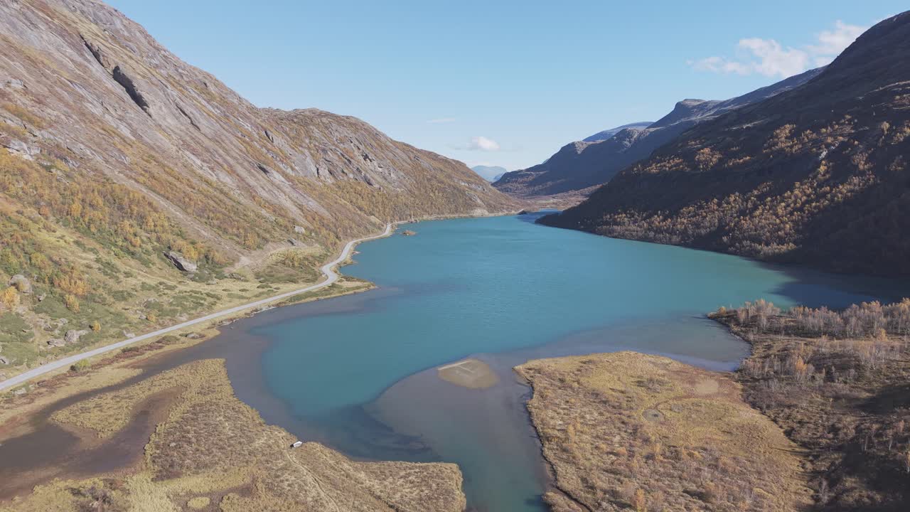 A drone-filmed view of a glacial lake with striking turquoise-green waters in Norway, surrounded by autumn mountains