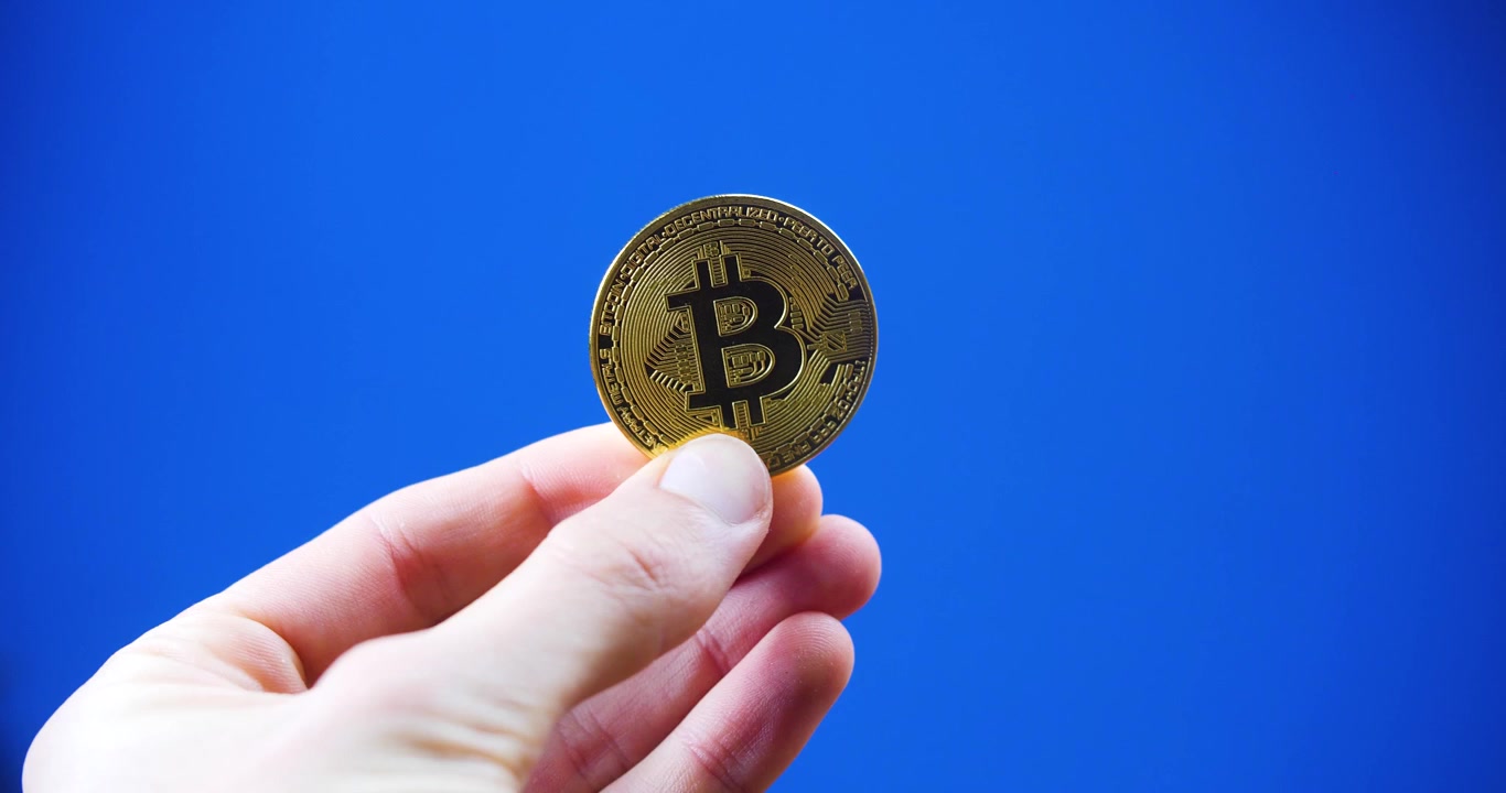 Dijital para birimini simgeleyen, parlak mavi bir arka plana karşı tutulan Bitcoin.