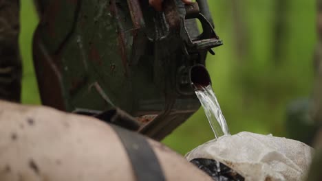 Military figure pours water on restrained person, closeup in outdoor setting