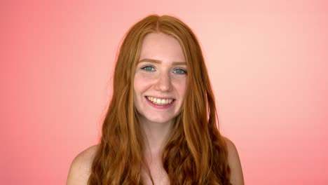 young redhead woman smiling and looking to camera, on pink background