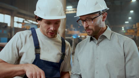 engineer discussing technical drawings with worker in industrial plant