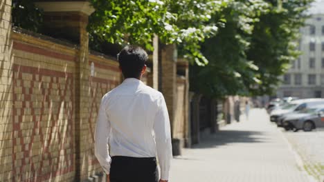 rear view of man wearing white shirt walking on riga streets, sunny day