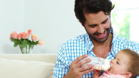 padre feliz sentado en un sofá y biberón alimentando a su bebé