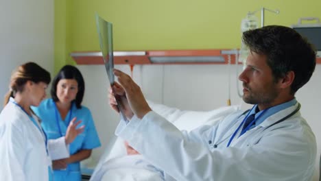 Doctor-examining-x-ray-while-nurse-interacting-with-patient-in-background