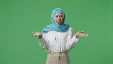 wondering asian muslim woman saying why and standing doubtfully in the green screen background studio