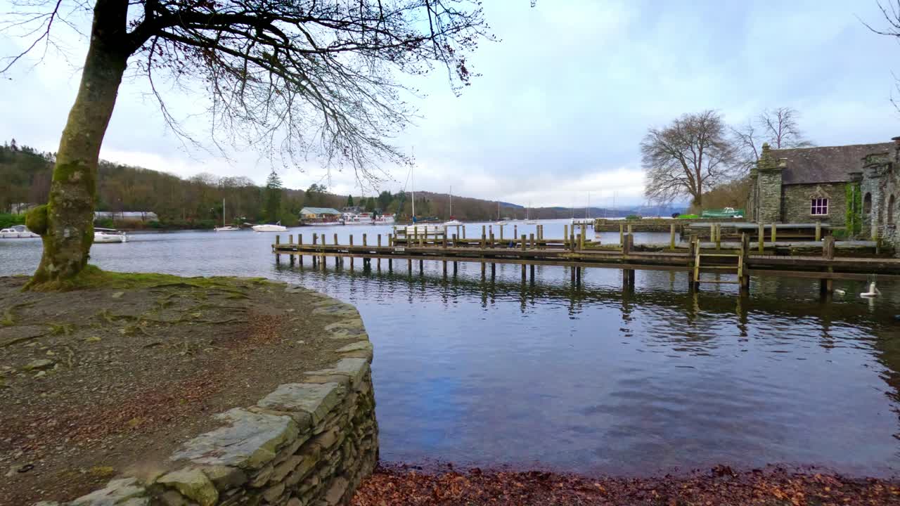 Lake Windermere i det engelske Lake District, med dens ikoniske træmole, historiske stenbyggede bygninger og stemningsfulde grå himmel