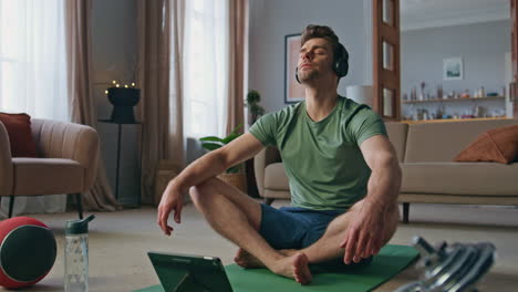 relaxed guy sitting lotus position in headphones at home. closed eyes yoga man