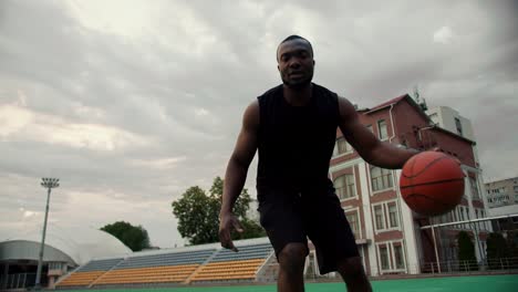 Black-skinned-basketball-player-in-black-sportswear-leads-a-basketball-on-a-sports-field-in-a-city-against-a-gray-sky