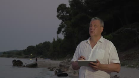 Älterer-Mann-Benutzt-Tablet-PC-Am-Späten-Abend-Am-Strand