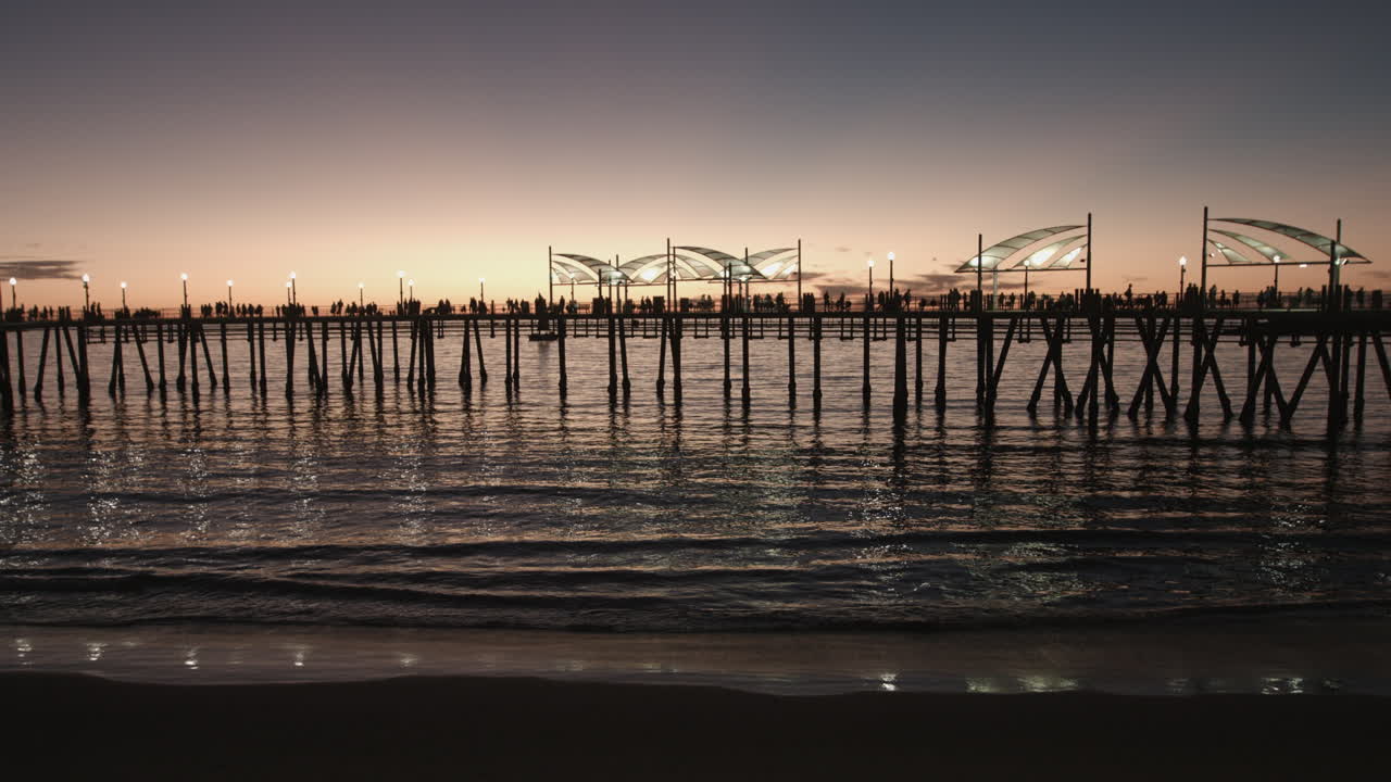 Sunset over the iconic Redondo Beach Pier with people fishing and strolling above the Pacific Ocean. Golden hour light reflects on the water, creating a vibrant Southern California coastal scene