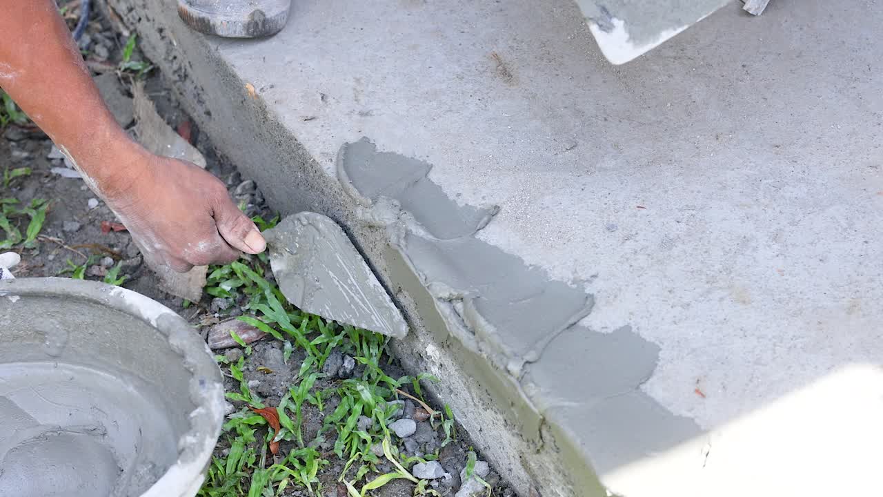 A worker smooths wet cement on a concrete surface in daylight, showcasing construction techniques in Phuket, Thailand