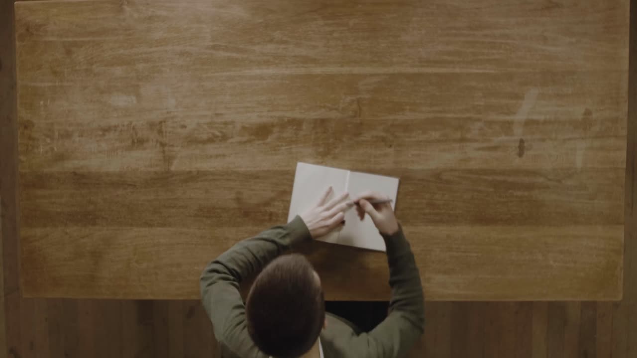 A Man Writing His Notes In His Diary On A Wooden Table - Top View Shot