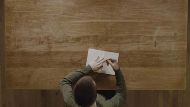 A Man Writing His Notes In His Diary On A Wooden Table - Top View Shot