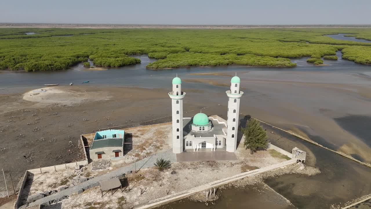 Drone aerial of Joal mosque in Senegal with tall white minarets, surrounded by lagoon and coastal village, symbolizing religion and African culture