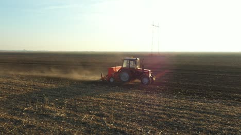 dolly orbit move in aerial top view of tractor as dragging a sowing machine over agricultural field, farmland