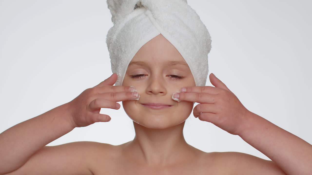 Lovely young child girl applying cleansing moisturizing face cream, skincare natural creme cosmetics