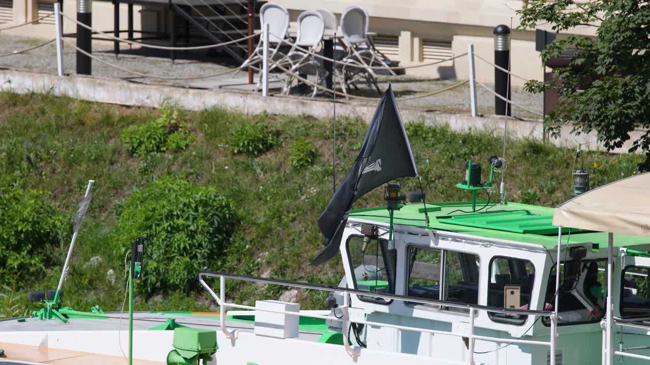 Pirate flag flutters atop green-roofed boat docked riverside in Prague, captured in daylight