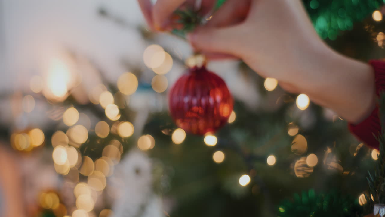 mujer recortada decorando árbol de navidad iluminado con adornos en casa