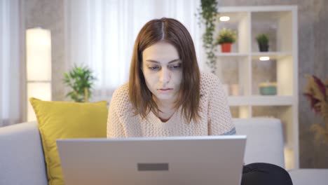 focused and serious young woman at home looking at laptop.