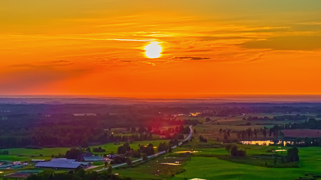 Setting sun over rural farmland under vivid evening sky, warm golden hues cast across countryside, space for text in sky