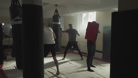 los deportistas entrenan golpes con bolsas de boxeo en el club deportivo. los kickboxers profesionales hacen ejercicios en equipo en el gimnasio de lucha en cámara lenta. ocio y actividad saludable
