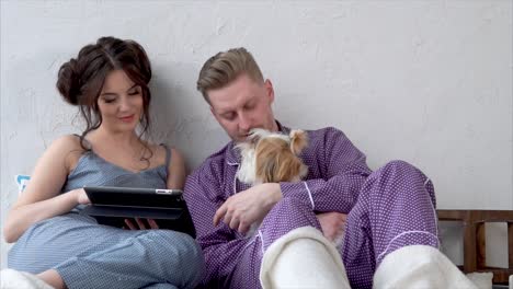 couple relaxing with a dog on bed with a tablet