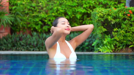 Atractiva-Mujer-Asiática-Joven-Acariciando-Su-Cabello-Mojado-En-Una-Piscina-De-Un-Complejo-Hotelero-De-Lujo,-Fotograma-Completo-A-Cámara-Lenta