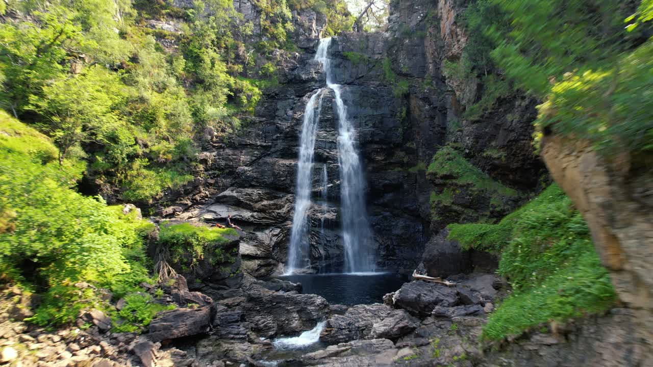 antena de aguas en cascada de cataratas humeantes en glen douchary con un hombre sentado en el borde de la roca