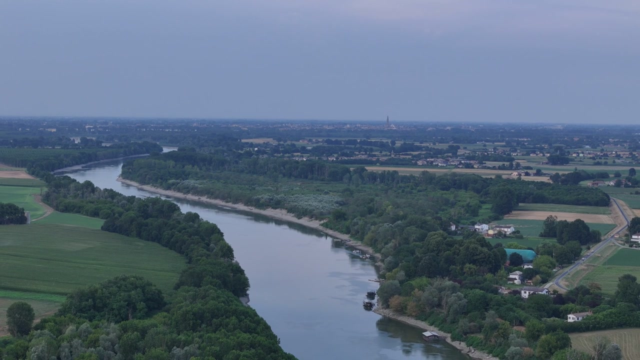 Fiume Po, Isola Serafini, Monticelli d'Ongina, Piacenza, Emilia-Romagna, Italia, che rivela lo skyline di Cremona, il Torrazzo, la foresta ripariale e la pianura alluvionale agricola durante l'ondata di calore del 2026.