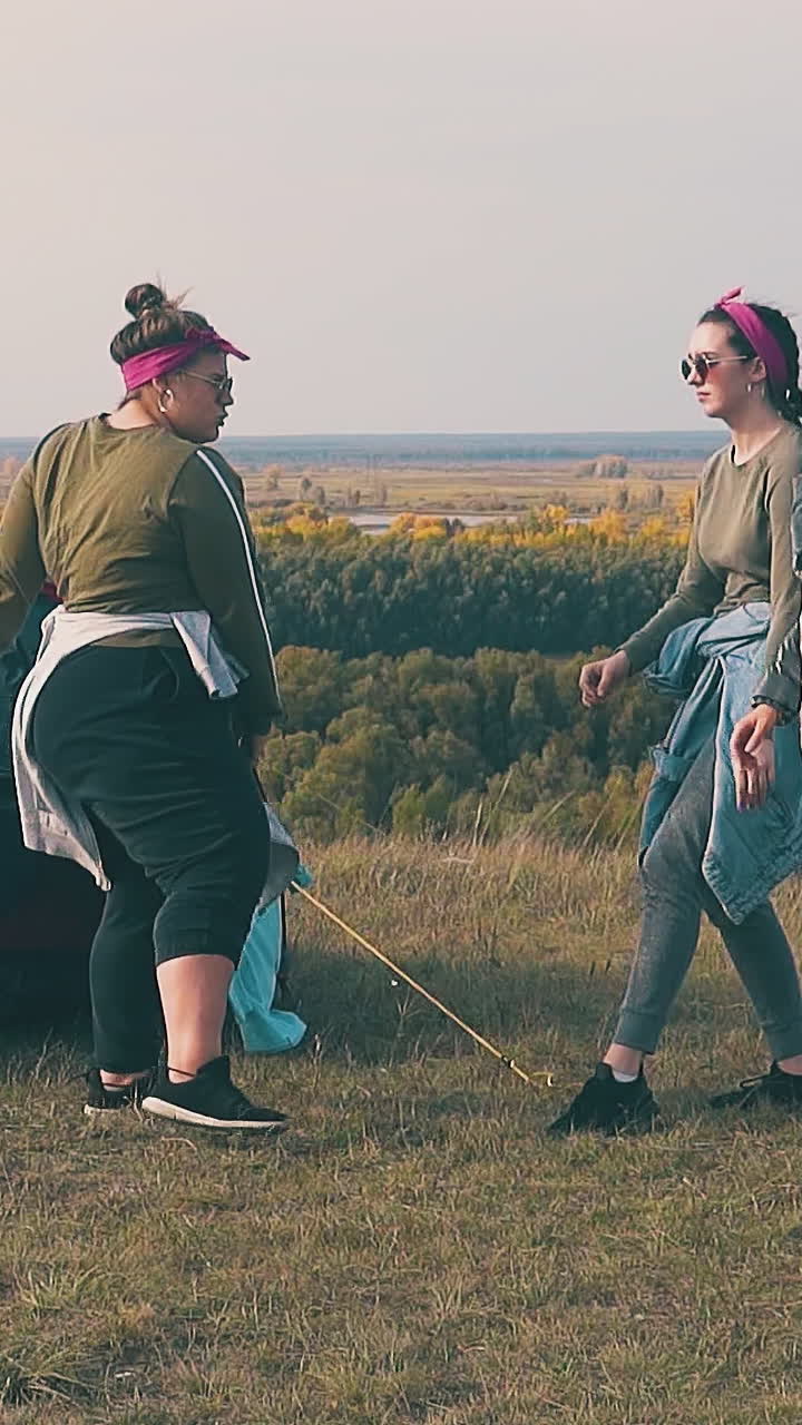 tipsy girls dance at blue tent having outdoor party against calm river near yellow autumn forest slow motion