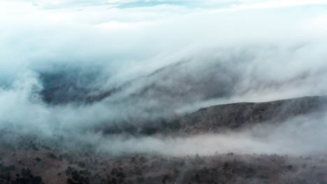 misty clouds rolling over a forested hillside, creating a serene, mysterious atmosphere, aerial view