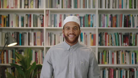 Un-Joven-Confiado-Del-Medio-Oriente-Parado-En-La-Biblioteca-Mirando-Un-Retrato-Sonriente-De-Un-Orgulloso-Empresario-Riendo