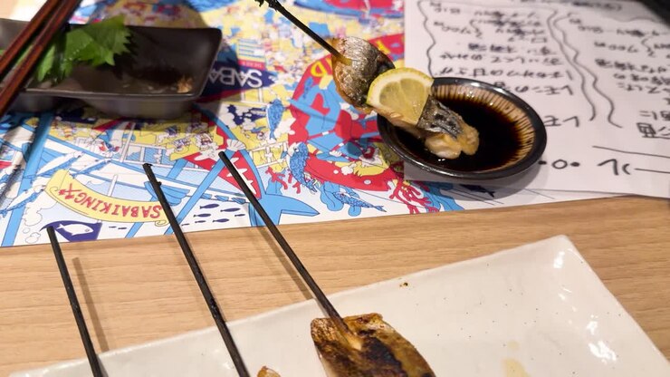 Una mano intinge spiedini di sgombro grigliato nella salsa di soia in un ristorante a Kanazawa, Giappone.