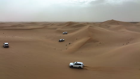 Aerial-view-of-4x4-off-road-trucks-driving-over-dunes-of-the-Dubai-Desert,-in-UAE