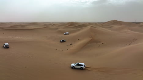 aerial view of 4x4 off road trucks driving over dunes of the dubai desert, in uae