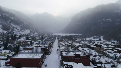 Filmische-Drohnenaufnahme-Aus-Der-Luft-Des-Skigebiets-Telluride-Mountain-In-Der-Innenstadt-Von-Colorado,-Neuschnee-Und-Nebel-Der-Malerischen-Berglandschaft-Und-Historischen-Gebäuden,-Lastwagen-Und-Autos,-Vorwärtsbewegung-Am-Morgen-Im-Winter