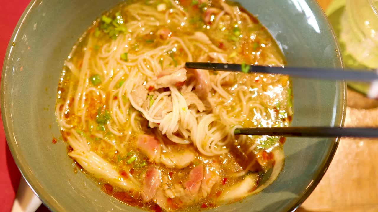 Chopsticks lift noodles from a flavorful broth in a Bangkok restaurant. Warm lighting enhances the inviting atmosphere