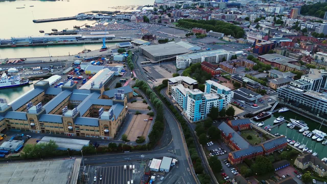 Low-angle aerial drone flies over Southampton city at autumn sunset, capturing trees, boats, and nearby sea, with warm golden light reflecting across the urban coastal landscape