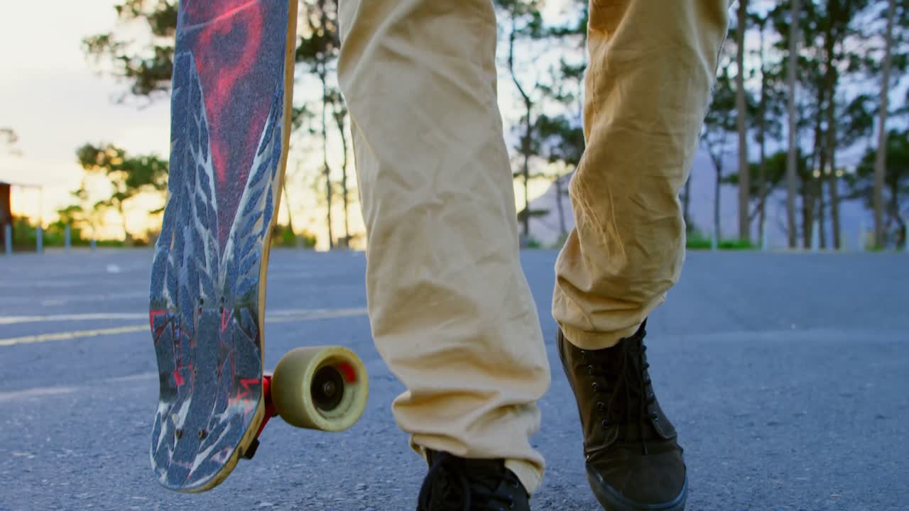 sección baja de un joven patinador masculino caminando con patineta en una carretera de campo 4k