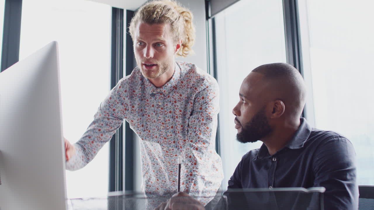 Two male colleagues in discussion at a computer monitor in a creative office, low angle, close up