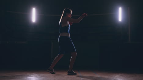 Boxer-woman-in-red-bandages-on-the-hands-of-and-blue-t-shirt-conducts-battle-with-of-practicing-the-speed-and-technique-strikes-hands.-Camera-movement-side-View.-Steadicam-shot